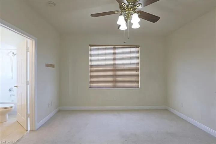 Neutral-toned interior featuring carpeting, a center ceiling fan with multi-bulb light fixture, a window with horizontal blinds, and a paneled interior door