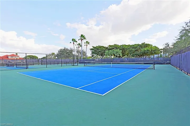 Hard-surfaced tennis court featuring perimeter chain-link fencing, dual-toned surfacing, and integrated net systems