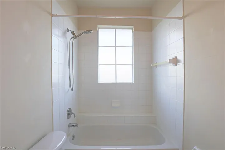Guest Bath Full-wall white ceramic tiling surrounding a porcelain soaking tub, integrated hand-held shower fixture, and a central privacy-glass window