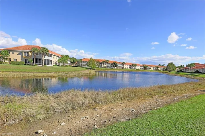 Multi-unit residential complex featuring terracotta-tiled roofs, stucco exterior finish, screened-in lanais, and mature landscaping situated along a waterfront pond