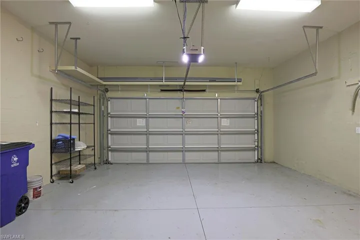 Two-car garage featuring a sectional overhead door, automated door opener, finished concrete flooring, and built-in ceiling-mounted storage shelving