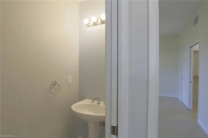 Pedestal sink with polished chrome faucet, circular wall-mounted towel ring, and three-bulb vanity light fixture
