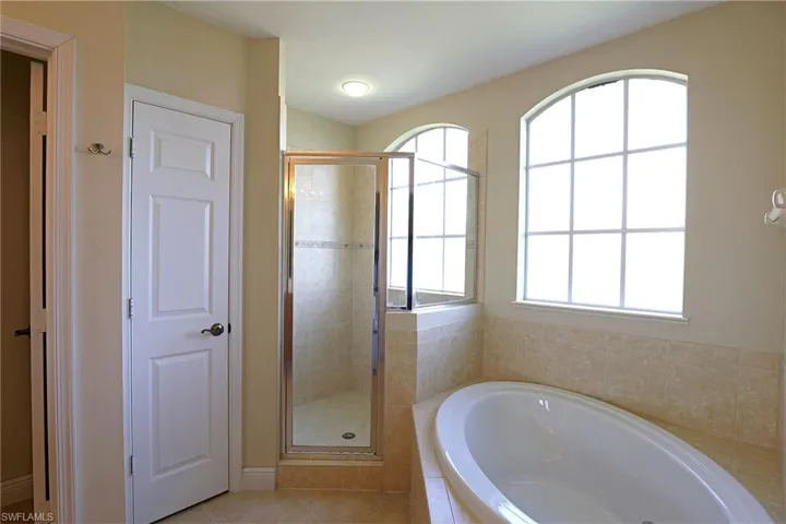 Bathroom featuring an oval soaking tub with a tiled surround, glass-enclosed shower, and arched grid-pane windows