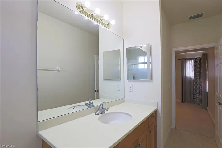 Vanity featuring wood-finish cabinetry, solid-surface countertop, integrated oval sink, wall-mounted mirror, and multi-bulb light fixture