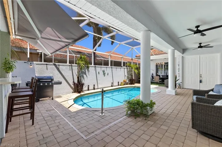 Covered patio featuring paver flooring, a screened pool enclosure, structural columns, and dual ceiling fans