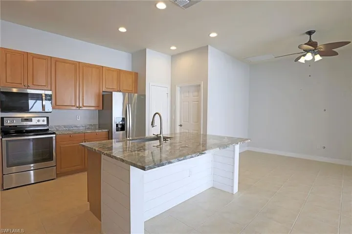 Kitchen featuring light wood cabinetry, stone countertops, stainless steel appliances, a center island with a shiplap base, and recessed lighting