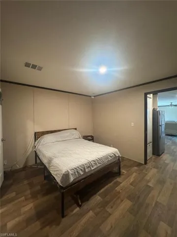 Bedroom featuring freestanding refrigerator, dark wood finished floors, and ornamental molding
