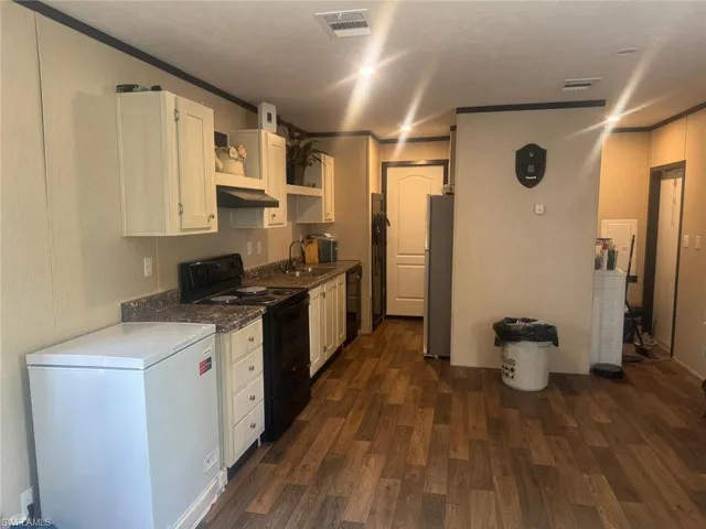 Kitchen with black appliances, dark wood-style floors, white cabinetry, open shelves, and crown molding