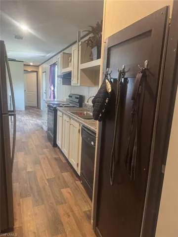 Kitchen with dark wood finished floors, black appliances, open shelves, and light countertops
