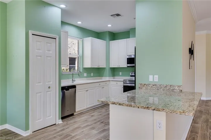Kitchen featuring a peninsula, white cabinets, wood tiled floors, light stone counters, and stainless steel appliances