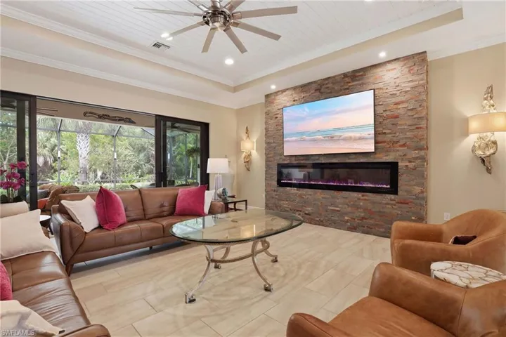 Living area featuring a ceiling fan, a stone fireplace, a wooden tray ceiling, recessed lighting, and crown molding