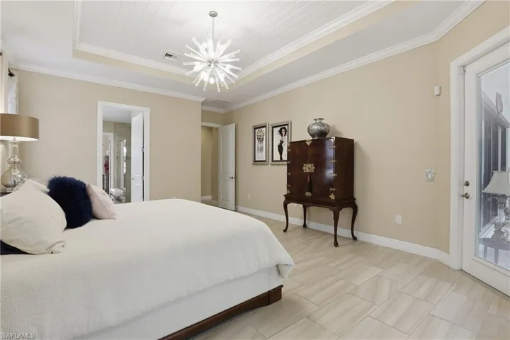 Bedroom featuring a raised ceiling, crown molding, access to outside, and a chandelier