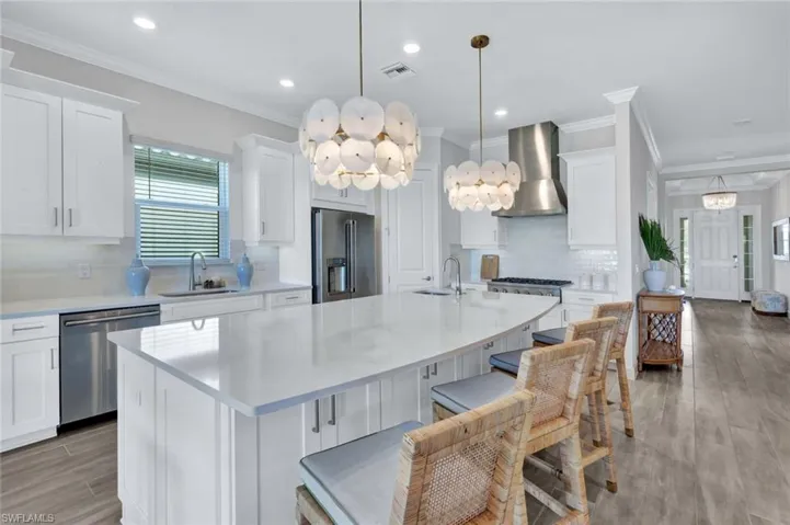 Kitchen with light countertops, a sink, visible vents, appliances with stainless steel finishes, and wall chimney exhaust hood