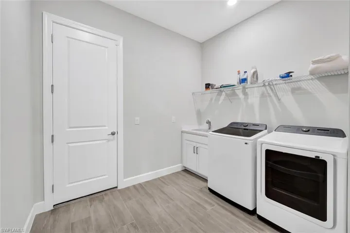 Washroom with washing machine and clothes dryer, light wood-style flooring, baseboards, a sink, and cabinet space