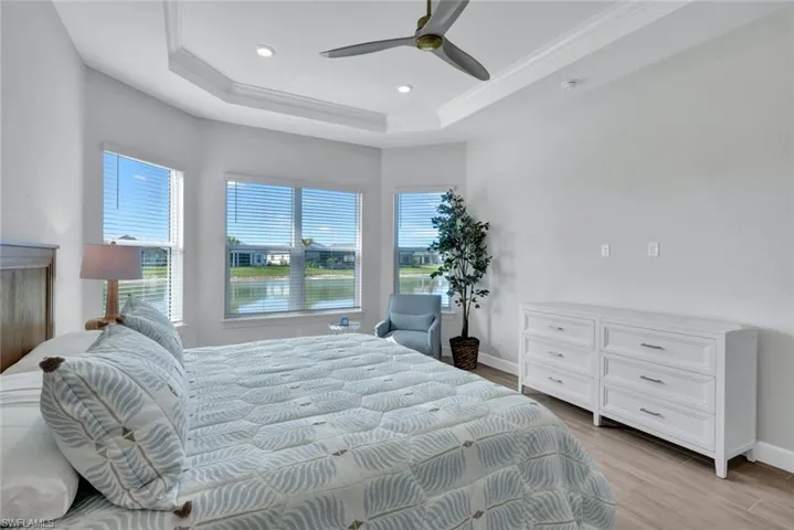 Bedroom with a tray ceiling, multiple windows, light wood finished floors, and baseboards