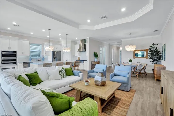 Living area with light wood-type flooring, a tray ceiling, visible vents, and a notable chandelier
