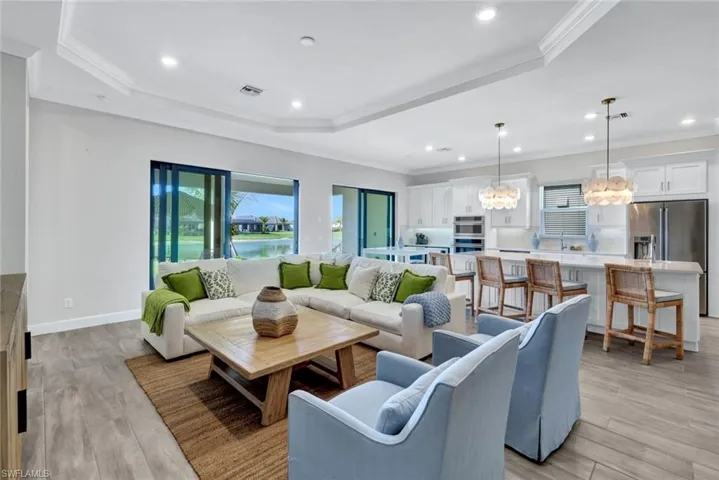 Living area with a tray ceiling, visible vents, light wood finished floors, and an inviting chandelier