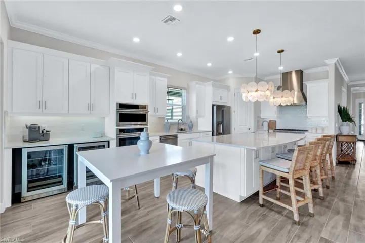 Kitchen featuring wall chimney range hood, appliances with stainless steel finishes, wine cooler, and visible vents