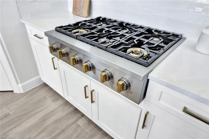 Interior details with white cabinetry, tasteful backsplash, stainless steel gas cooktop, light wood-style floors, and light stone countertops