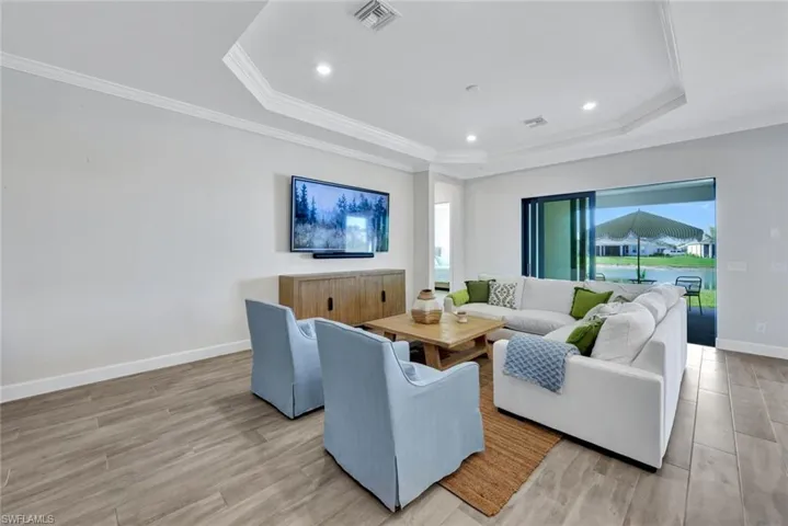 Living room with visible vents, baseboards, ornamental molding, light wood-type flooring, and a tray ceiling