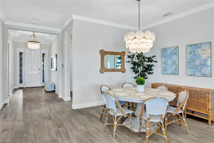 Dining space featuring visible vents, crown molding, baseboards, wood finished floors, and a notable chandelier