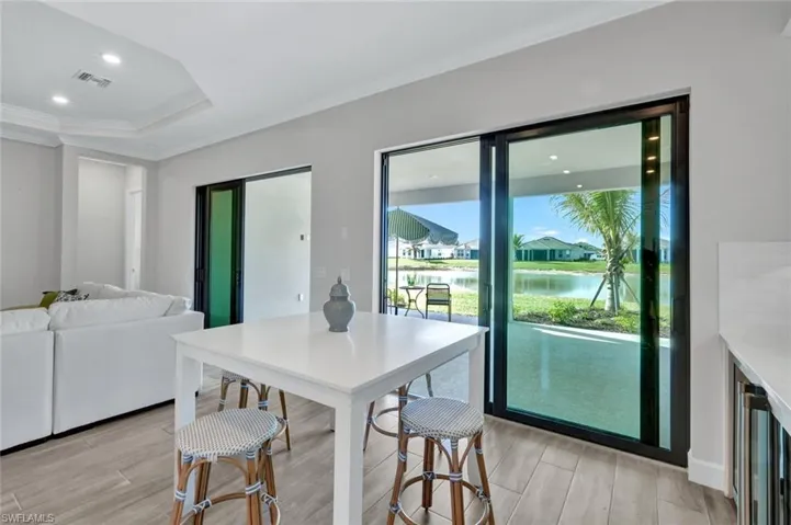 Dining area with crown molding, a water view, a raised ceiling, visible vents, and light wood-style flooring