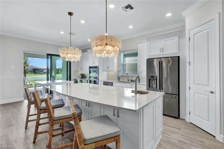 Kitchen featuring ornamental molding, a sink, visible vents, a kitchen island with sink, and appliances with stainless steel finishes