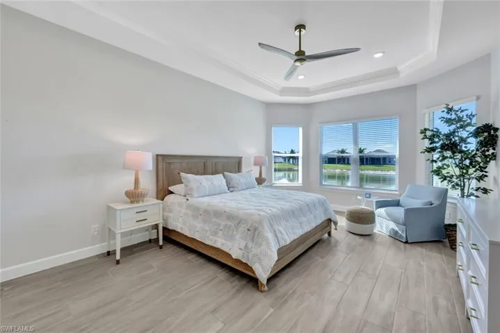 Bedroom with baseboards, ceiling fan, ornamental molding, light wood-type flooring, and a tray ceiling
