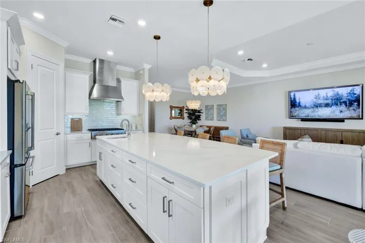 Kitchen with open floor plan, light countertops, visible vents, freestanding refrigerator, and wall chimney exhaust hood