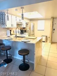 Kitchen with stainless steel microwave, under cabinet range hood, light tile patterned flooring, freestanding refrigerator, and a peninsula