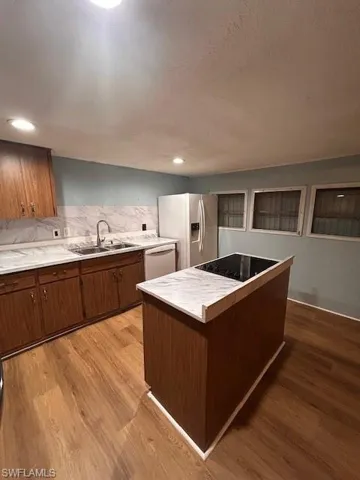 Kitchen featuring hardwood / wood-style floors, tasteful backsplash, a kitchen island, appliances with stainless steel finishes, and sink