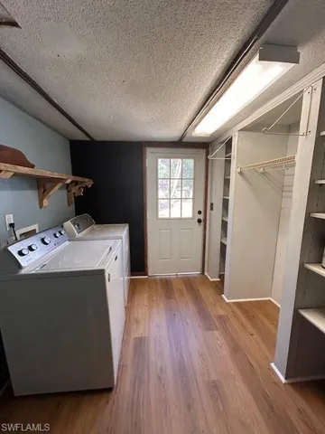 Laundry room with washer and clothes dryer, light hardwood / wood-style flooring, and a textured ceiling