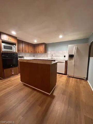 Kitchen featuring light wood-type flooring, refrigerator, backsplash, wall oven, and dishwashing machine