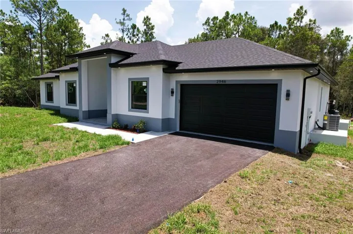 View of front of property featuring a garage, a front lawn, and central AC unit