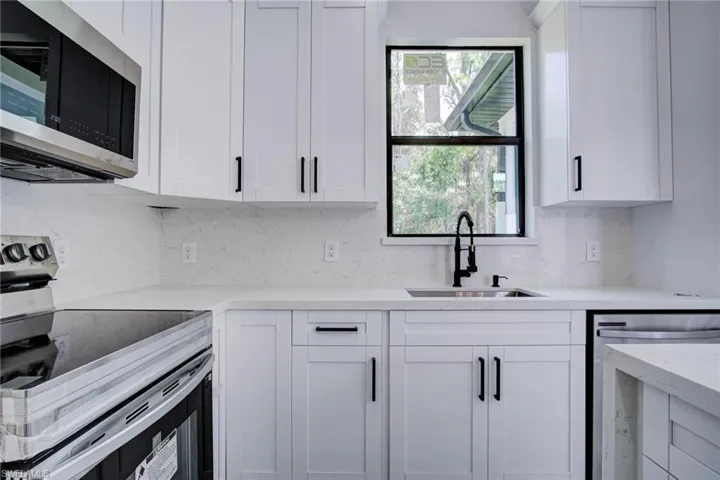 Kitchen featuring decorative backsplash, sink, stainless steel appliances, and white cabinets