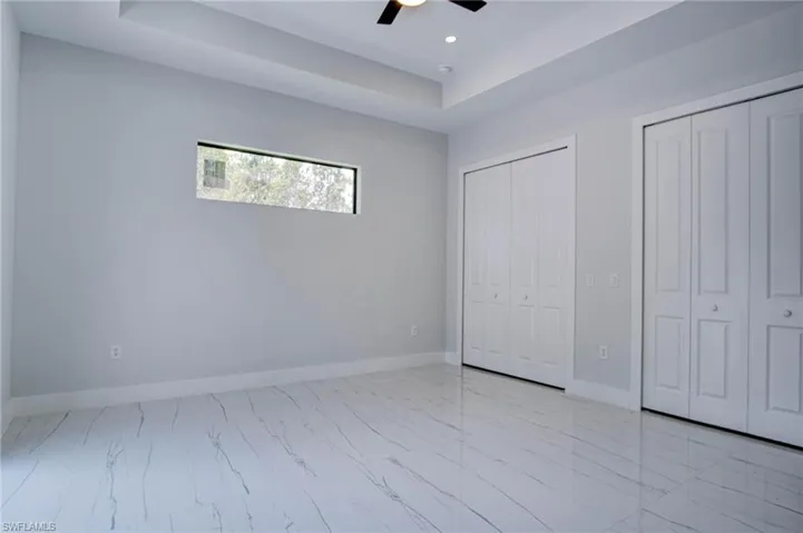 Unfurnished bedroom featuring two closets, a raised ceiling, light tile patterned floors, and ceiling fan