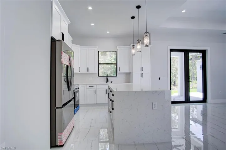 Kitchen featuring light tile patterned flooring, stainless steel refrigerator, white cabinets, decorative backsplash, and pendant lighting