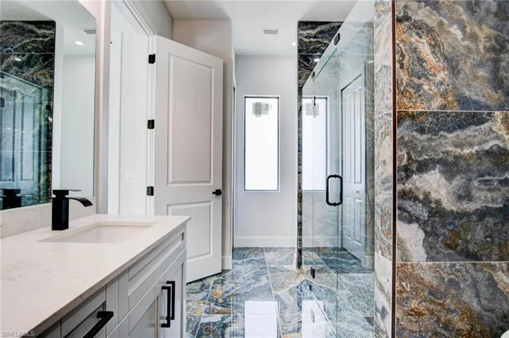 Bathroom with a shower with shower door, tile patterned floors, and vanity
