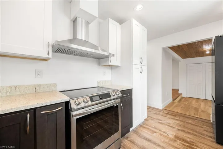 Kitchen with light wood-type flooring, white cabinetry, wall chimney exhaust hood, and electric range