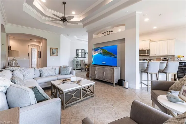 Living area with arched walkways, ceiling fan, crown molding, a tray ceiling, and light tile patterned floors