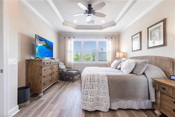 Bedroom with wood finished floors, a tray ceiling, ornamental molding, ceiling fan, and recessed lighting