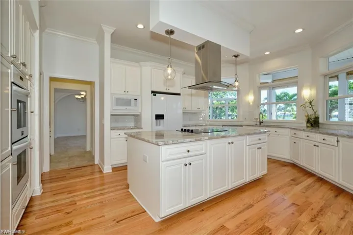 Kitchen with island exhaust hood, white appliances, a center island, white cabinetry, and hanging light fixtures