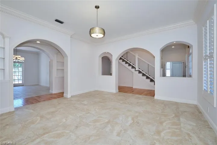 Unfurnished room featuring built in shelves, light hardwood / wood-style floors, crown molding, and a notable chandelier