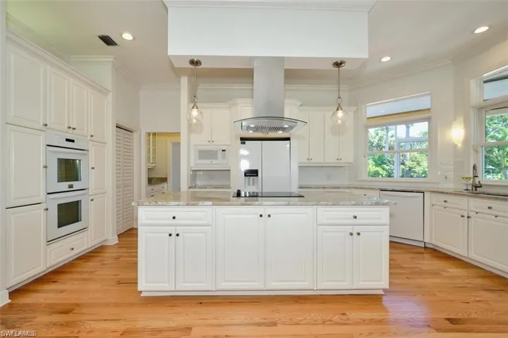 Kitchen with white cabinets, light hardwood / wood-style floors, white appliances, and island exhaust hood