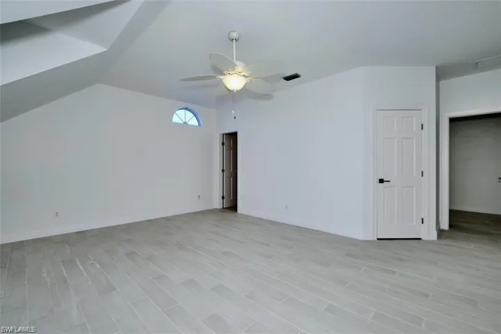 Empty room with ceiling fan, lofted ceiling, and light wood-type flooring