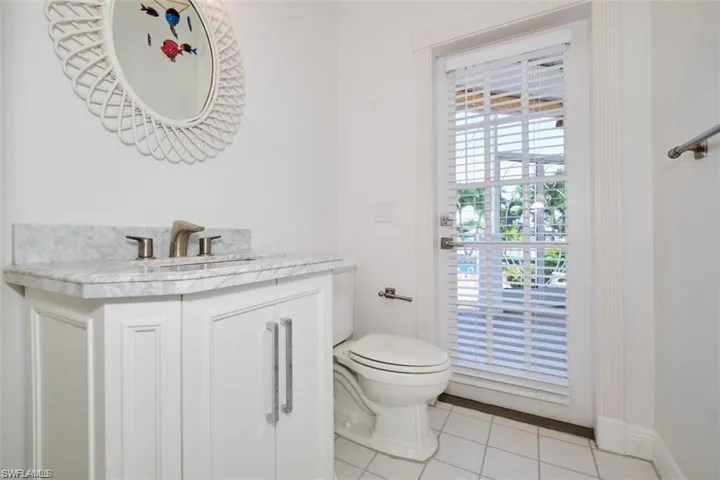 1/2 bath off pool and hallway, featuring tile patterned flooring, vanity, and toilet