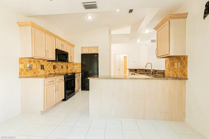 Kitchen with light brown cabinetry, decorative backsplash, a peninsula, dark stone countertops, and lofted ceiling