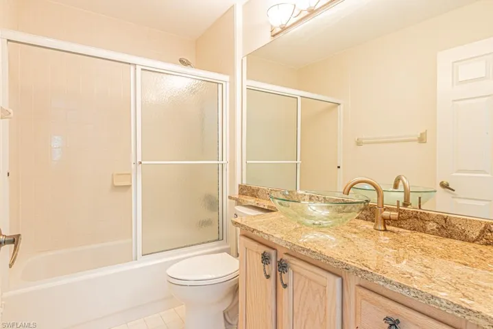 Full bath with vanity, light tile patterned floors, and bath / shower combo with glass door