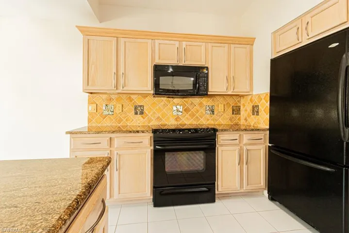 Kitchen with light brown cabinetry, black appliances, tasteful backsplash, and light stone countertops