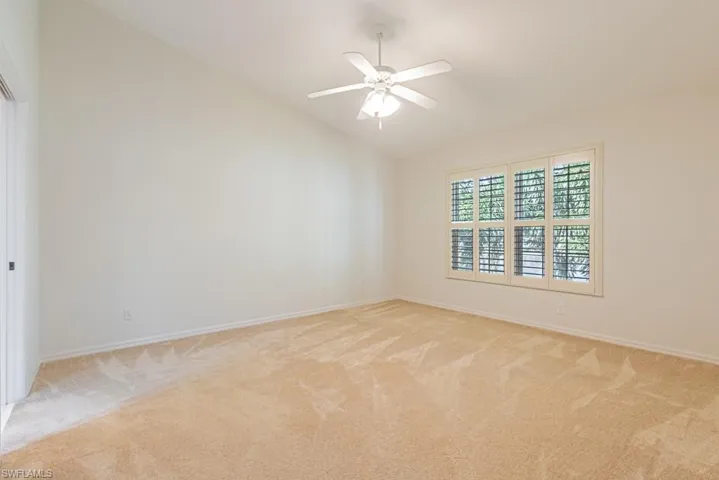 Empty room with light carpet, vaulted ceiling, and a ceiling fan